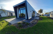 Moderne lodge met een hellend dak, grote ramen en een groen gazon onder een heldere blauwe lucht.