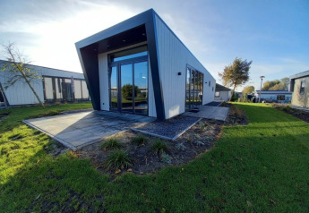 Moderne lodge med skråt tag og store vinduer, omgivet af grønt græs og en klar blå himmel.