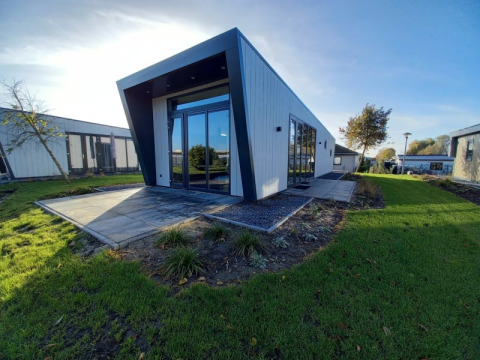 Moderne lodge met een hellend dak, grote ramen en een groen gazon onder een heldere blauwe lucht.