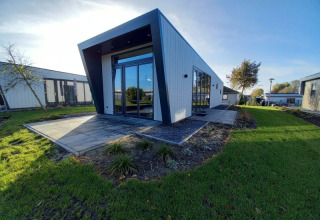 Moderne lodge met een hellend dak, grote ramen en een groen gazon onder een heldere blauwe lucht.