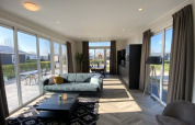 Moderne lodge woonkamer met grote ramen, een zetel, salontafel en uitzicht op een zonnig terras.