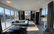 Moderne lodge woonkamer met grote ramen, bank, salontafel en uitzicht op een zonnig terras buiten.