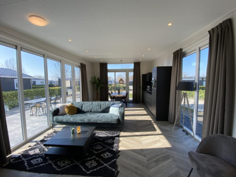 Moderne lodge woonkamer met grote ramen, bank, salontafel en uitzicht op een zonnig terras buiten.