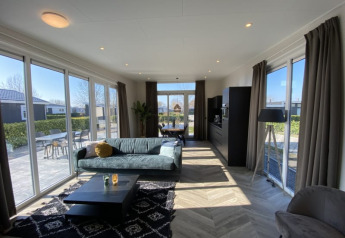 Moderne lodge woonkamer met grote ramen, bank, salontafel en uitzicht op een zonnig terras buiten.