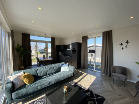 Moderne lodge woonkamer met grote ramen, groene bank, zwarte keuken, eettafel en veel daglicht.