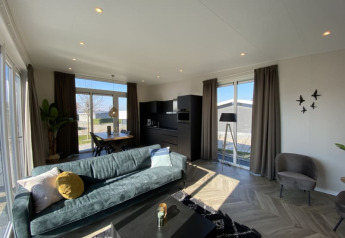 Moderne lodge woonkamer met grote ramen, groene bank, zwarte keuken, eettafel en veel daglicht.