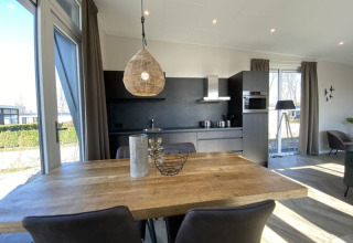 Interior de un lodge moderno con mesa de comedor, cocina elegante y grandes ventanales con luz natural.