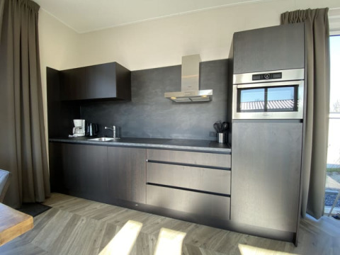 Cocina moderna en una cabaña con muebles oscuros, horno integrado, cafetera y luz natural.