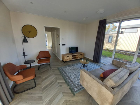 Soggiorno di un lodge con grandi finestre, due poltrone arancioni, divano beige e pavimento in legno.