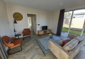 Soggiorno di un lodge con grandi finestre, due poltrone arancioni, divano beige e pavimento in legno.