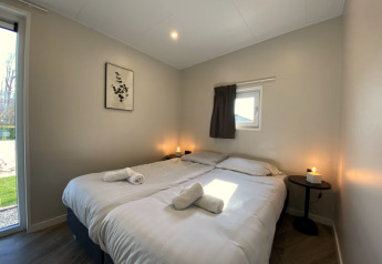 Modern lodge bedroom with two single beds, white linens, candles on nightstands, and sunlight through window.