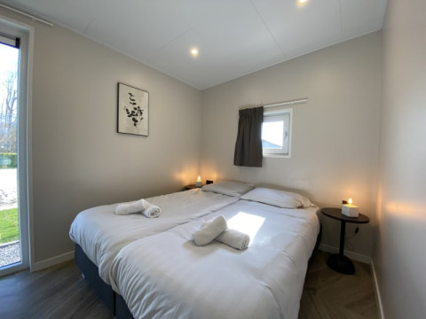 Modernes Lodge-Schlafzimmer mit zwei Einzelbetten, weißer Bettwäsche, Kerzen und einem Fenster im Tageslicht.