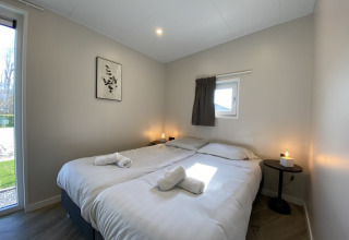Modernes Lodge-Schlafzimmer mit zwei Einzelbetten, weißer Bettwäsche, Kerzen und einem Fenster im Tageslicht.