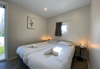 Modern lodge slaapkamer met twee eenpersoonsbedden, wit beddengoed, kaarsen en natuurlijk daglicht binnen.