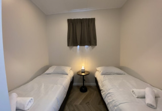 Chambre de lodge simple avec deux lits simples, du linge blanc, une table centrale et une petite fenêtre.