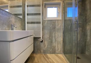 Baño moderno de lodge con ducha de vidrio, radiador toallero de pared, lavabo y gran espejo.