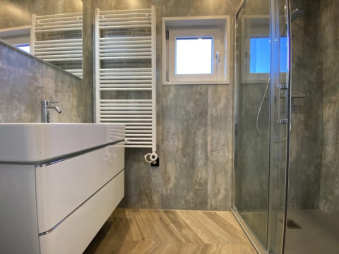 Salle de bain moderne de lodge avec douche en verre, radiateur sèche-serviettes, lavabo et grand miroir.