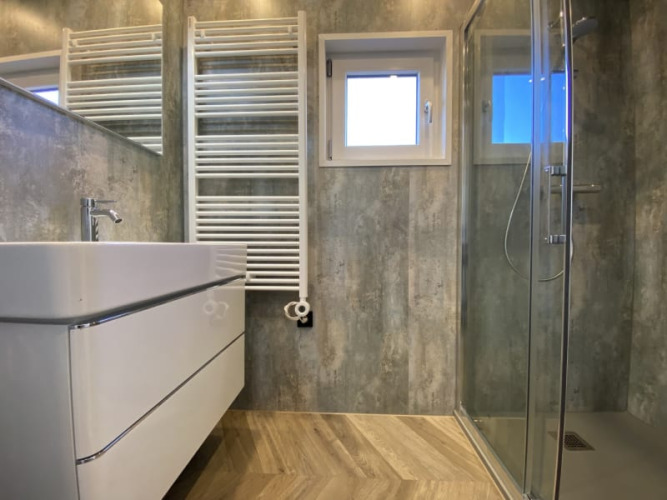 Baño moderno de lodge con ducha de vidrio, radiador toallero de pared, lavabo y gran espejo.