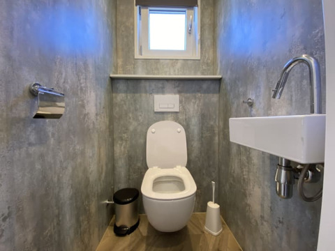 Bagno di lodge moderno con WC sospeso, piccolo lavandino, finestra, porta carta e spazzolone.