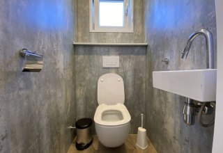 Bagno di lodge moderno con WC sospeso, piccolo lavandino, finestra, porta carta e spazzolone.