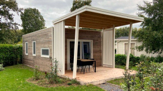 Cozy wooden lodge with a covered porch, outdoor dining area, and lush green surroundings in a garden.