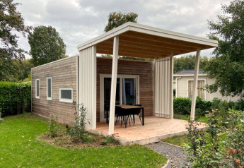 Cozy wooden lodge with a covered porch, outdoor dining area, and lush green surroundings in a garden.