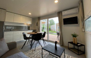 Modern glamping accommodation living space with kitchenette, dining table and patio view through glass doors.