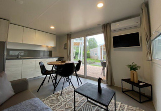Modern glamping accommodation living space with kitchenette, dining table and patio view through glass doors.