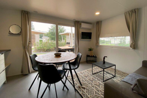 Lichte glampingaccommodatie met ronde eettafel, zwarte stoelen, salontafel en ramen met tuinzicht.