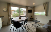 Bright glamping accommodation with round dining table, black chairs, coffee table, and garden view windows.