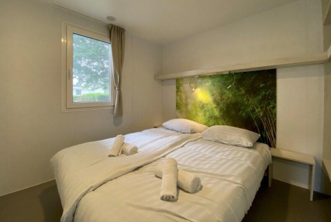 Chambre de glamping douillette avec lit double, draps blancs, serviettes roulées et tête de lit nature.