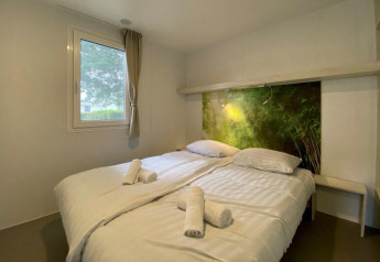 Accogliente stanza glamping con letto matrimoniale, lenzuola bianche, asciugamani e testiera verde.