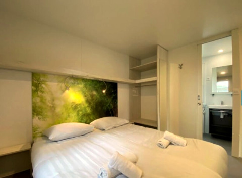Slaapkamer in een glamping-accommodatie met tweepersoonsbed, open kast, natuurkunst en badkamer.