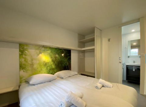 Bedroom in a glamping accommodation with double bed, open closet, nature wall art, and bathroom access.