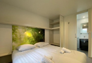 Chambre dans un hébergement glamping avec lit double, placard ouvert, art mural nature et accès à la salle de bain.