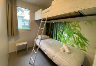 Lichte glampingkamer met stapelbed, raam, natuurbehang en minimalistisch meubilair voor een comfortabel verblijf.