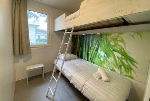 Habitación glamping luminosa con litera, ventana, papel pintado de naturaleza y mobiliario minimalista.