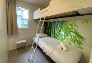 Habitación glamping luminosa con litera, ventana, papel pintado de naturaleza y mobiliario minimalista.