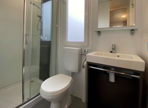 Moderne badkamer bij een glampinglocatie met glazen douche, toilet, wastafel en raam met daglicht.