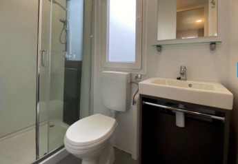 Modern bathroom at a glamping site with a glass shower, toilet, sink and window letting in natural light.
