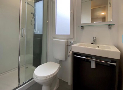 Moderne badkamer bij een glampingverblijf met glazen douchecabine, wc, lavabo en daglicht via raam.