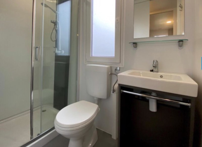 Baño moderno en alojamiento glamping con ducha de cristal, inodoro, lavabo y ventana con luz natural.