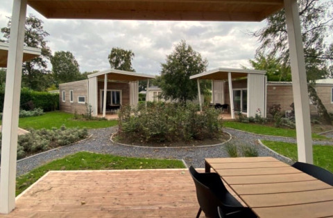 Foto van moderne glampingverblijven met houten veranda’s, grindpaden en veel groen rondom de huisjes.