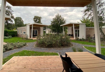 Photo of modern glamping cabins with wooden decks, garden paths, and greenery in a landscaped setting.