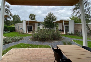 Photo of modern glamping cabins with wooden decks, garden paths, and greenery in a landscaped setting.