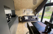 Moderne lodge met keukenhoek, grijze zetel, eettafel en grote ramen met zicht op het gazon.