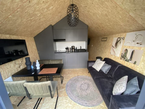 Interior de lodge moderno con sofá negro, mesa de comedor, cocina pequeña y decoración elegante en pared.