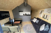Moderne lodge met zwarte bank, eettafel, kitchenette en stijlvolle decoraties aan OSB wandpanelen.