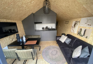 Interior de lodge moderno con sofá negro, mesa de comedor, cocina pequeña y decoración elegante en pared.