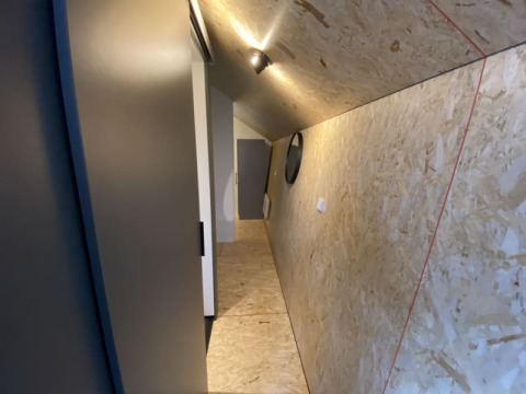 Pasillo inclinado en un lodge con paredes y techo de madera, iluminación moderna y una puerta al fondo.